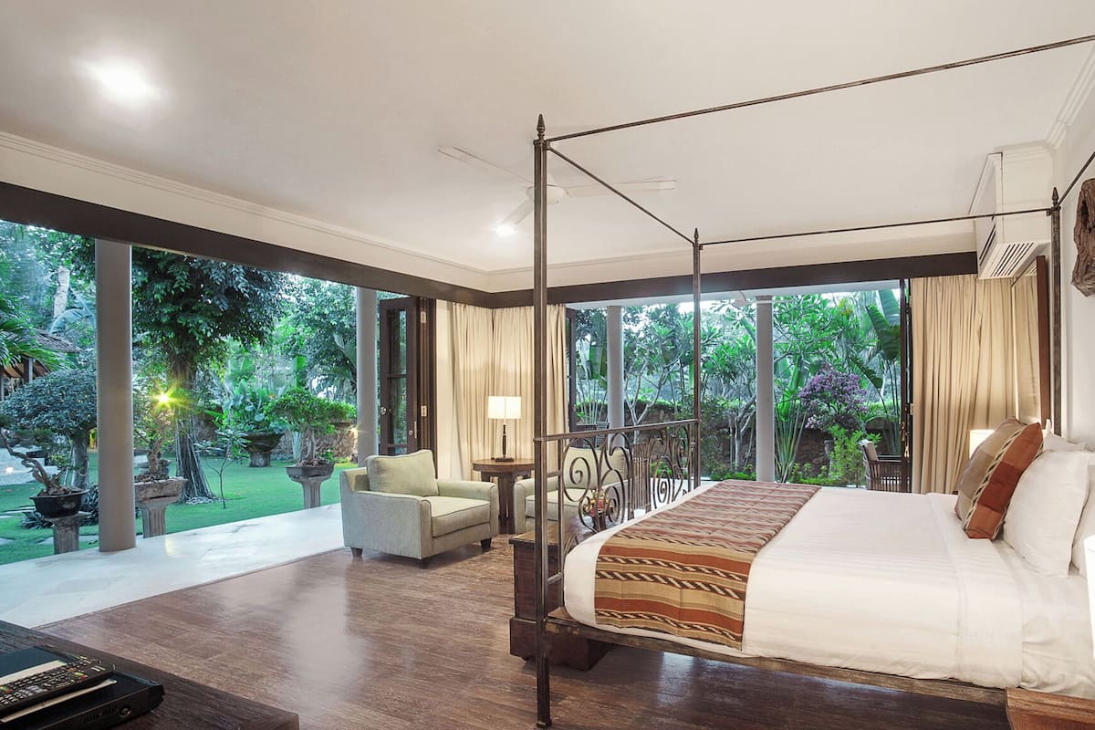 A spacious bedroom with a four-poster bed, large windows, and a view of a lush garden.