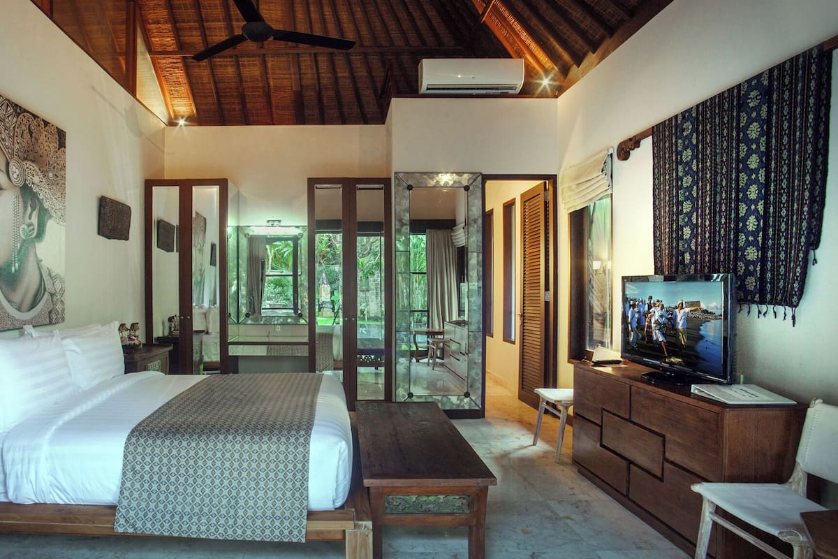 A bedroom with a large bed, a wooden desk, a television, and a large mirror.