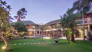 A courtyard with a pool, palm trees, and a two-story building with balconies. - Villa Avalon (Canggu)