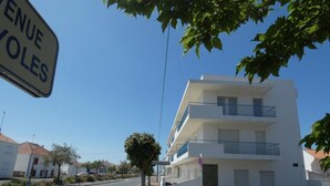 Ein mehrstöckiges weißes Gebäude mit Balkonen, blauem Himmel und einer Straße mit Zebrastreifen.