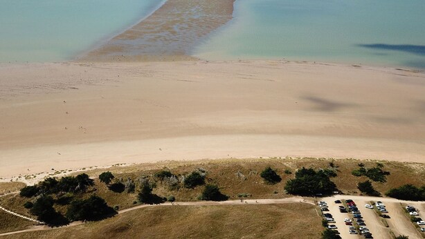 Luftaufnahme eines Strandes mit Parkplatz und spärlicher Vegetation.