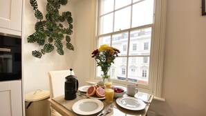 A breakfast table with plates, cutlery, a coffee pot, and a vase with flowers. - Stylish Apartments in Pimlico (London)