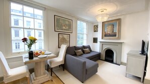 A living room with a fireplace, a sofa, a dining table with chairs, and a TV. - Stylish Apartments in Pimlico (London)