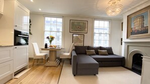 A modern living room with a grey sofa, white chairs, a dining table with a vase of flowers, and a fireplace. - Stylish Apartments in Pimlico (London)
