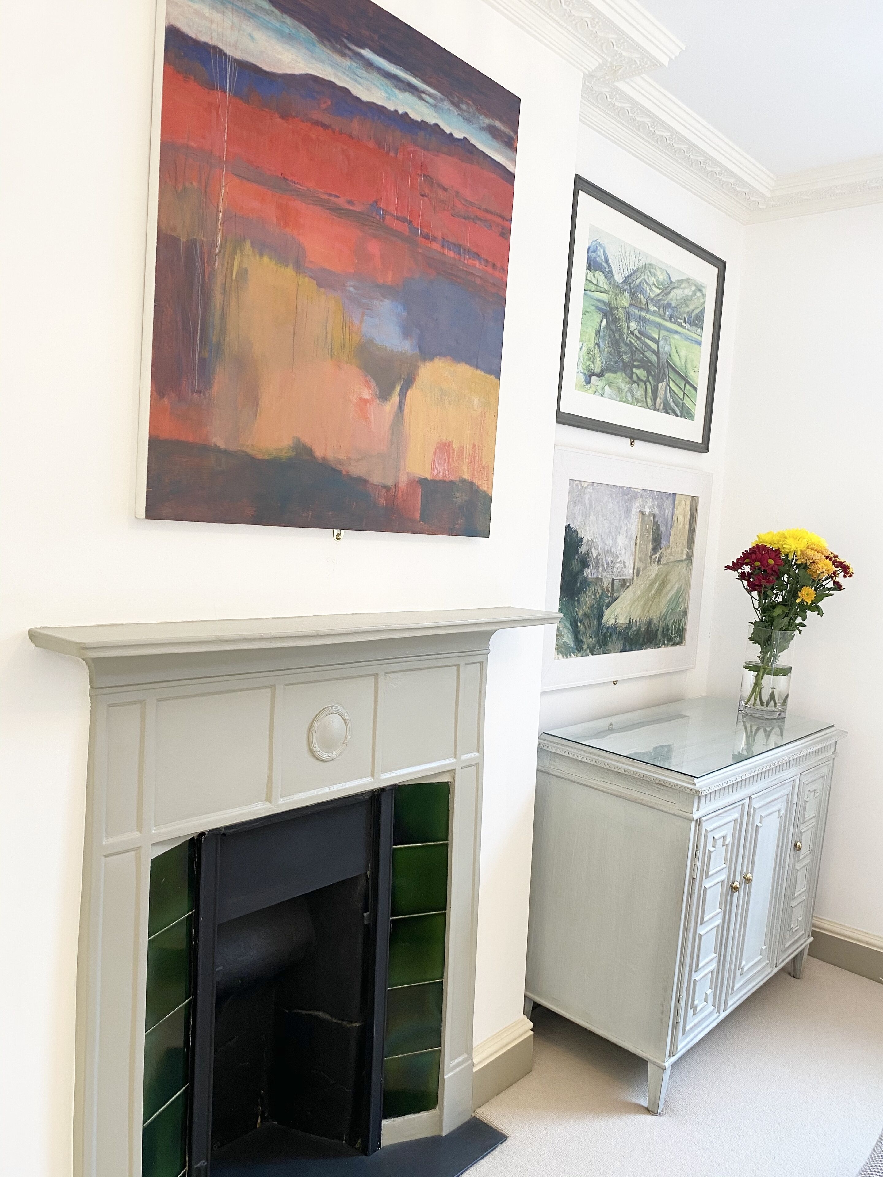 Una habitación con chimenea, un armario y tres cuadros en la pared.