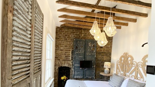 A bedroom with a large bed, wooden beams, a brick wall, a fireplace, and a chandelier. - Stylish Apartments in Pimlico (London)