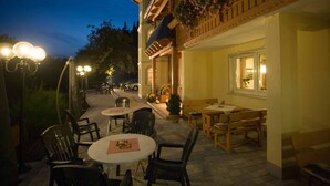 An outdoor patio with tables and chairs, a building with a balcony, and a street in the background.
