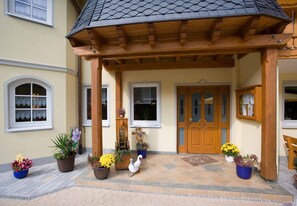Une entrée abritée, agrémentée d’une pergola en bois, d’une porte blanche et de plantes en pot.