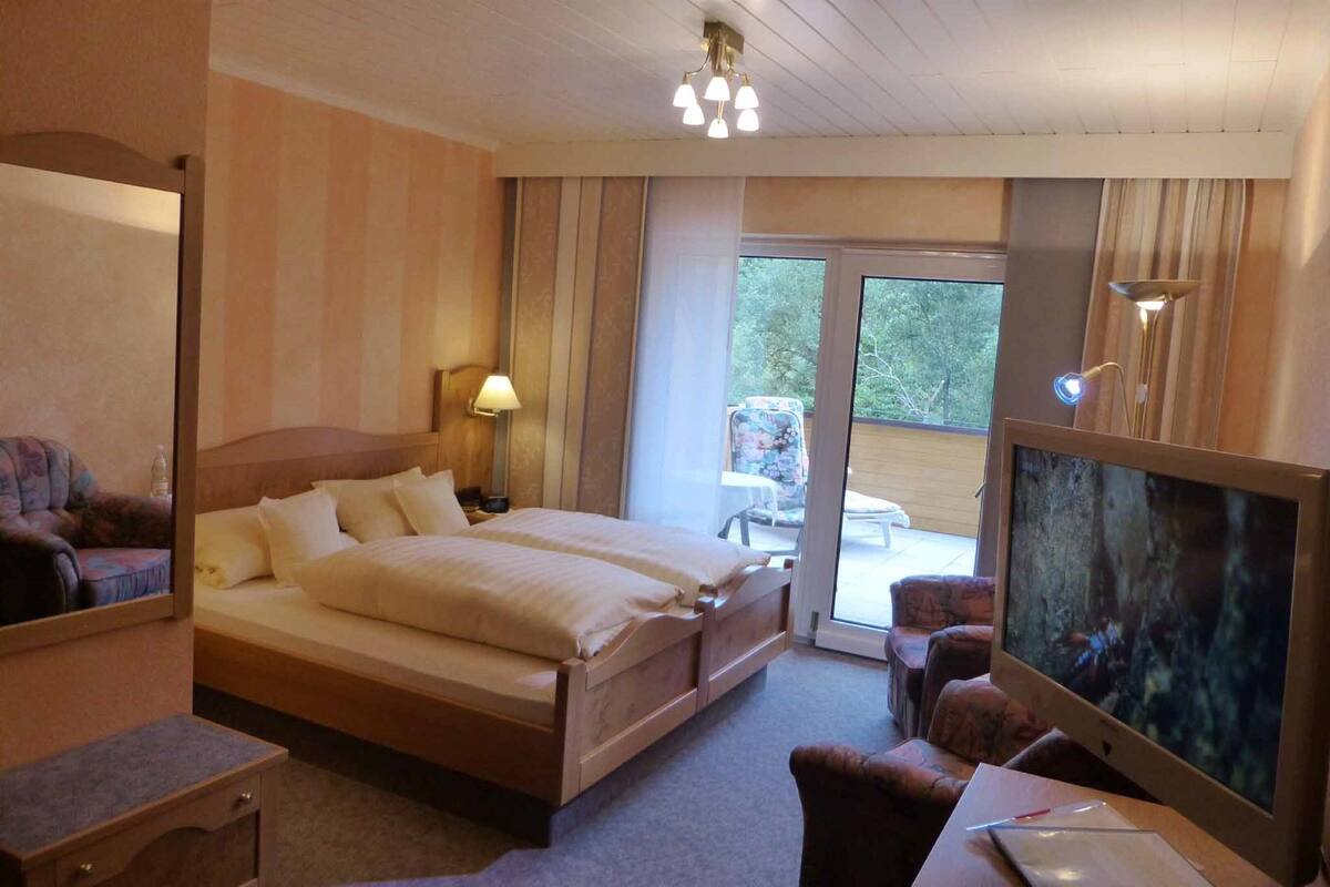 Une chambre d’hôtel avec un grand lit, un bureau avec un ordinateur, une télévision et un balcon donnant sur l’extérieur.