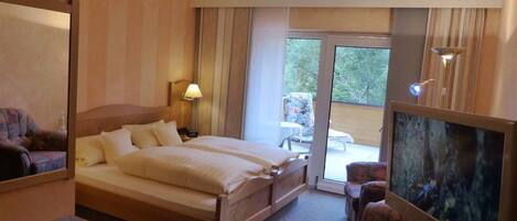 Habitación de hotel con una cama grande, un escritorio con ordenador, televisión y balcón con vistas al exterior.