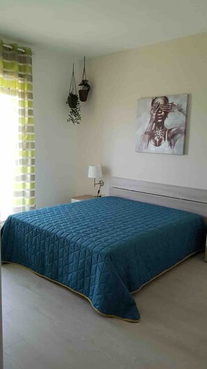Une chambre à coucher avec un lit, une table de chevet, une lampe, une plante suspendue et un tableau au mur.