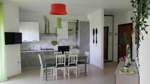 A modern kitchen with white cabinets, a dining table with chairs, and a red hanging light fixture. - 28 · Appartamento sul mare (Marina Julia)