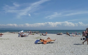A pebbled beach with people sunbathing and swimming, a clear sky, and a calm sea. - 28 · Appartamento sul mare (Marina Julia)
