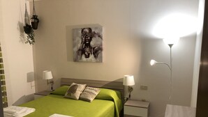 Quarto de hotel com cama, duas luminárias de cabeceira, mesa de cabeceira, pintura pendurada na parede e abajur.