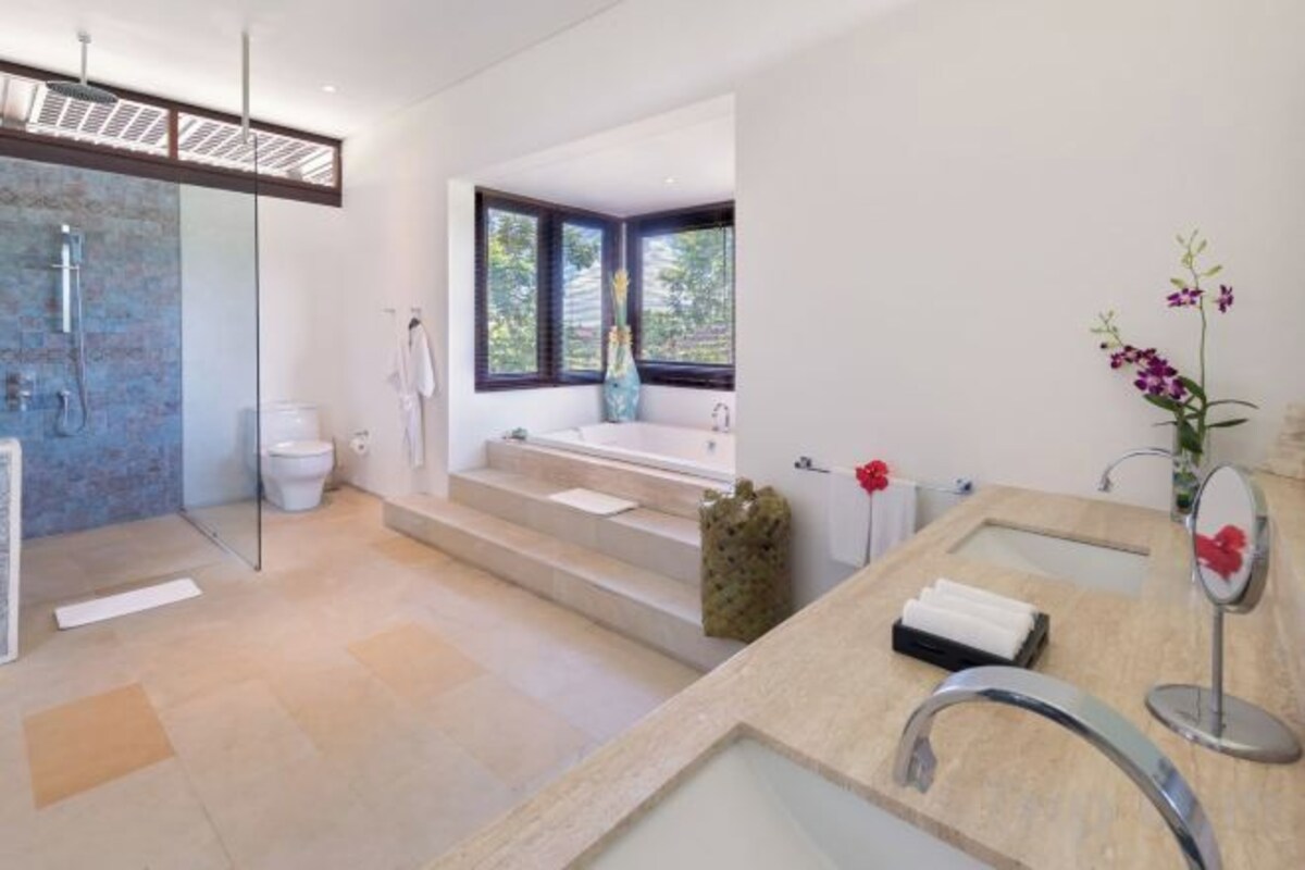A modern bathroom with a glass shower enclosure, a bathtub, and a large window.