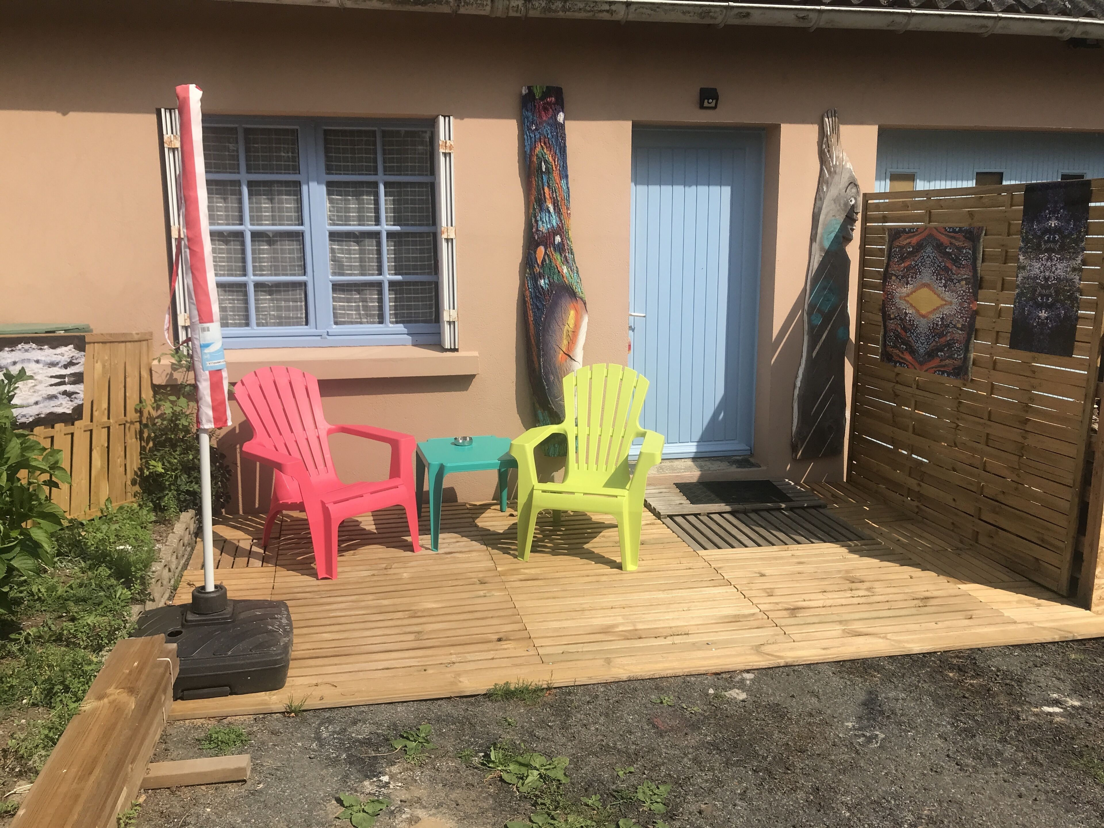 Un espacio al aire libre con piso de madera, una puerta azul y sillas coloridas.
