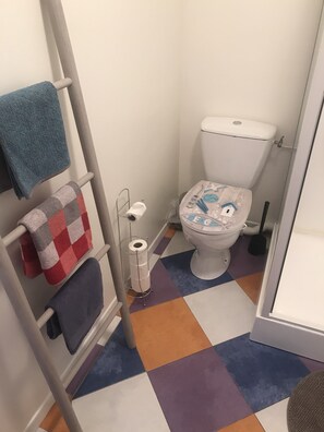 A small bathroom with a toilet, a towel rack with multiple towels, a toilet paper holder, and a colorful floor. - Arty, self-contained accomodation on "la cote de granit rose" 800m from the Breton sea (louannec)