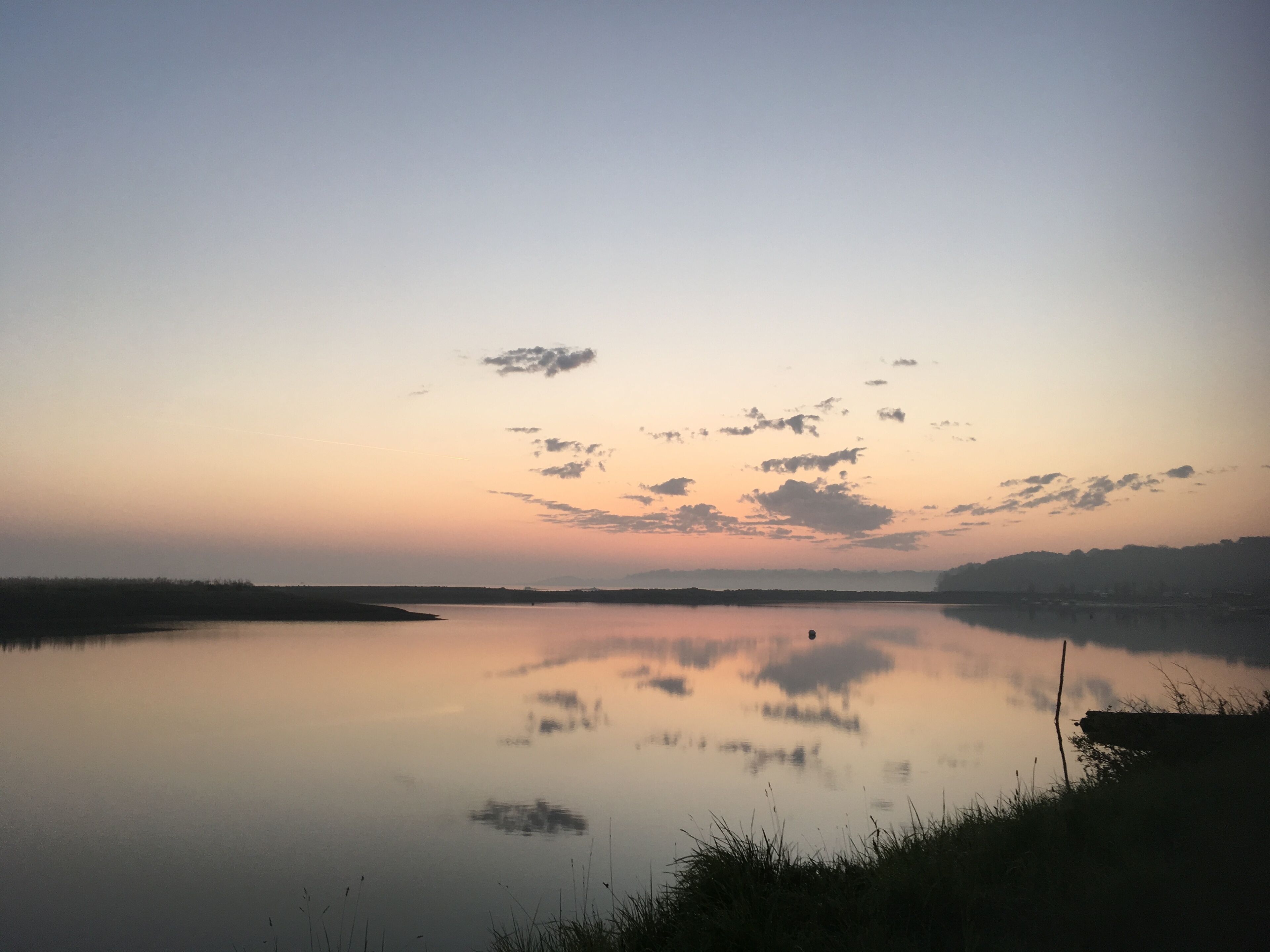 Un lago tranquilo al atardecer con cielo despejado y tierra lejana.