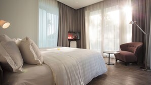Quarto de hotel moderno com uma cama grande, televisão, escrivaninha e uma cadeira.
