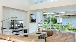 Uma sala de estar moderna com uma janela grande, uma televisão de tela plana, um sofá e uma escada que leva a um andar superior.