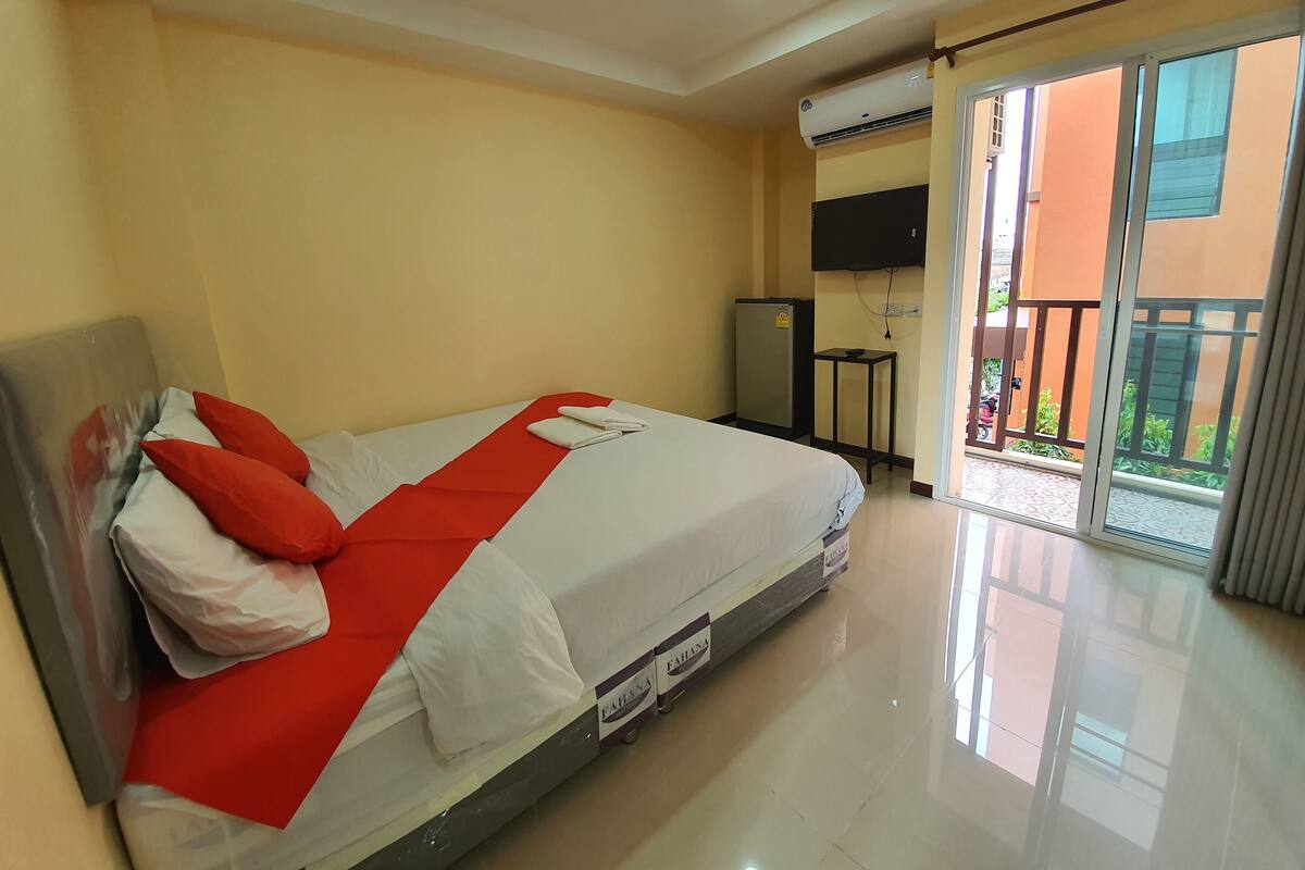 A hotel room with a bed, a TV, a refrigerator, and a balcony with a view.