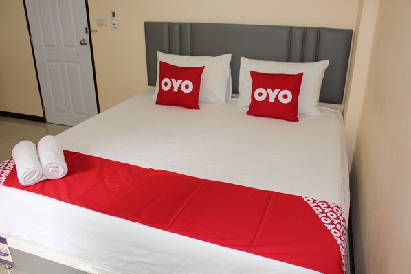 A hotel room with a bed, two pillows with the word 'OYO' on them, a red and white bedspread, and two rolled towels.
