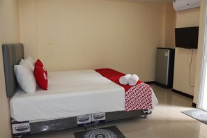A hotel room with a bed, pillows, a blanket, a towel, a refrigerator, and a television. - Awa Don Muang (Bangkok)