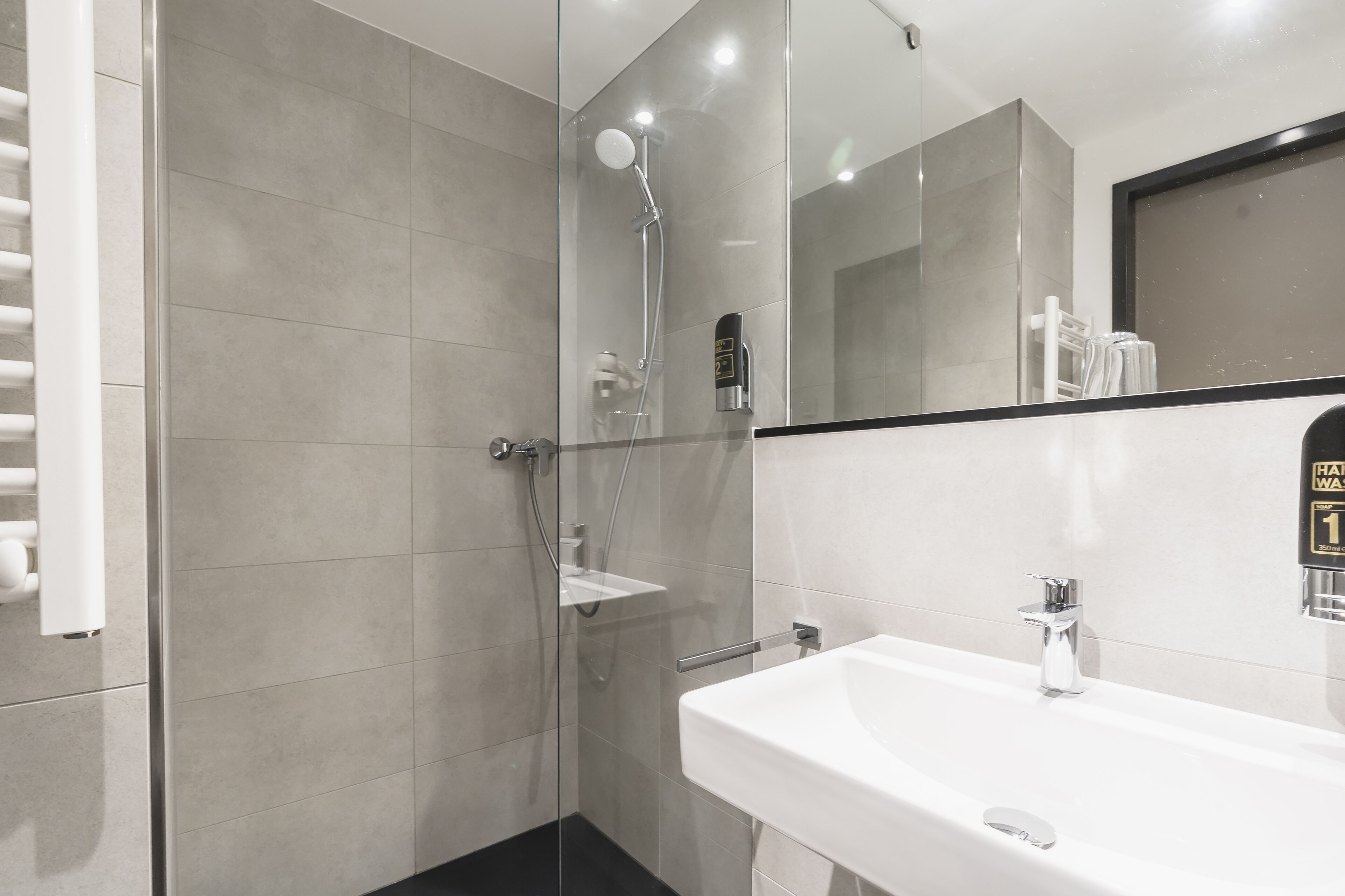 A modern bathroom with a glass-enclosed shower, a white sink, and a mirror with a black frame.