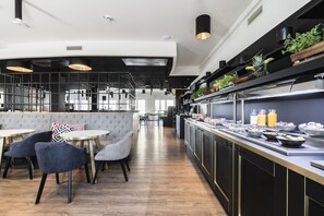 Un restaurante moderno con área de bar, asientos con sillas acolchadas y una barra con alimentos y bebidas.