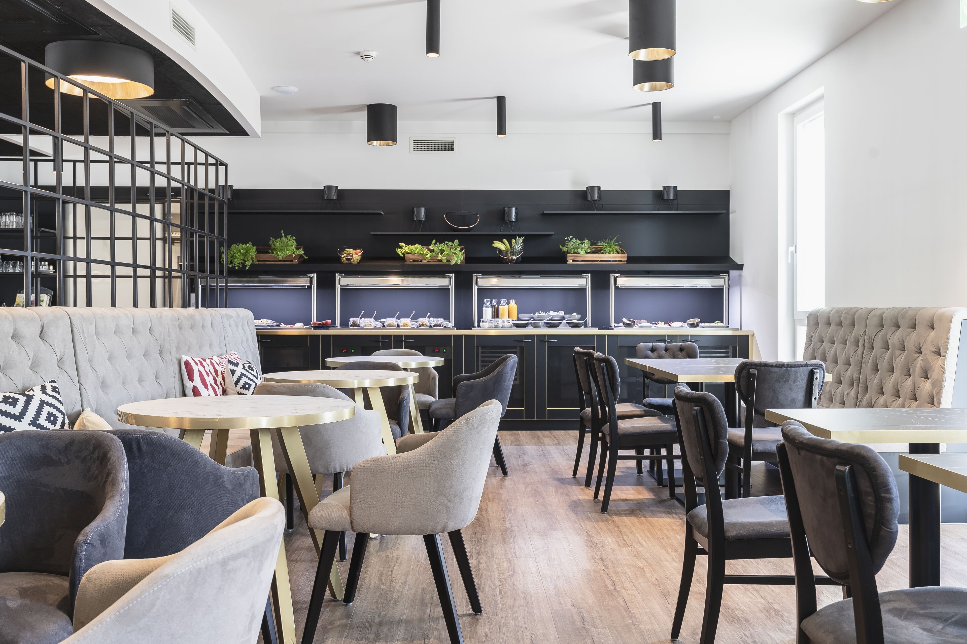 Un restaurant moderne avec des tables rondes et des chaises rembourrées, une décoration aux couleurs noir et blanc, et un escalier menant à une mezzanine.