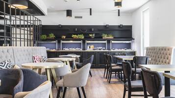 Un restaurant moderne avec des tables rondes et des chaises rembourrées, une décoration aux couleurs noir et blanc, et un escalier menant à une mezzanine.