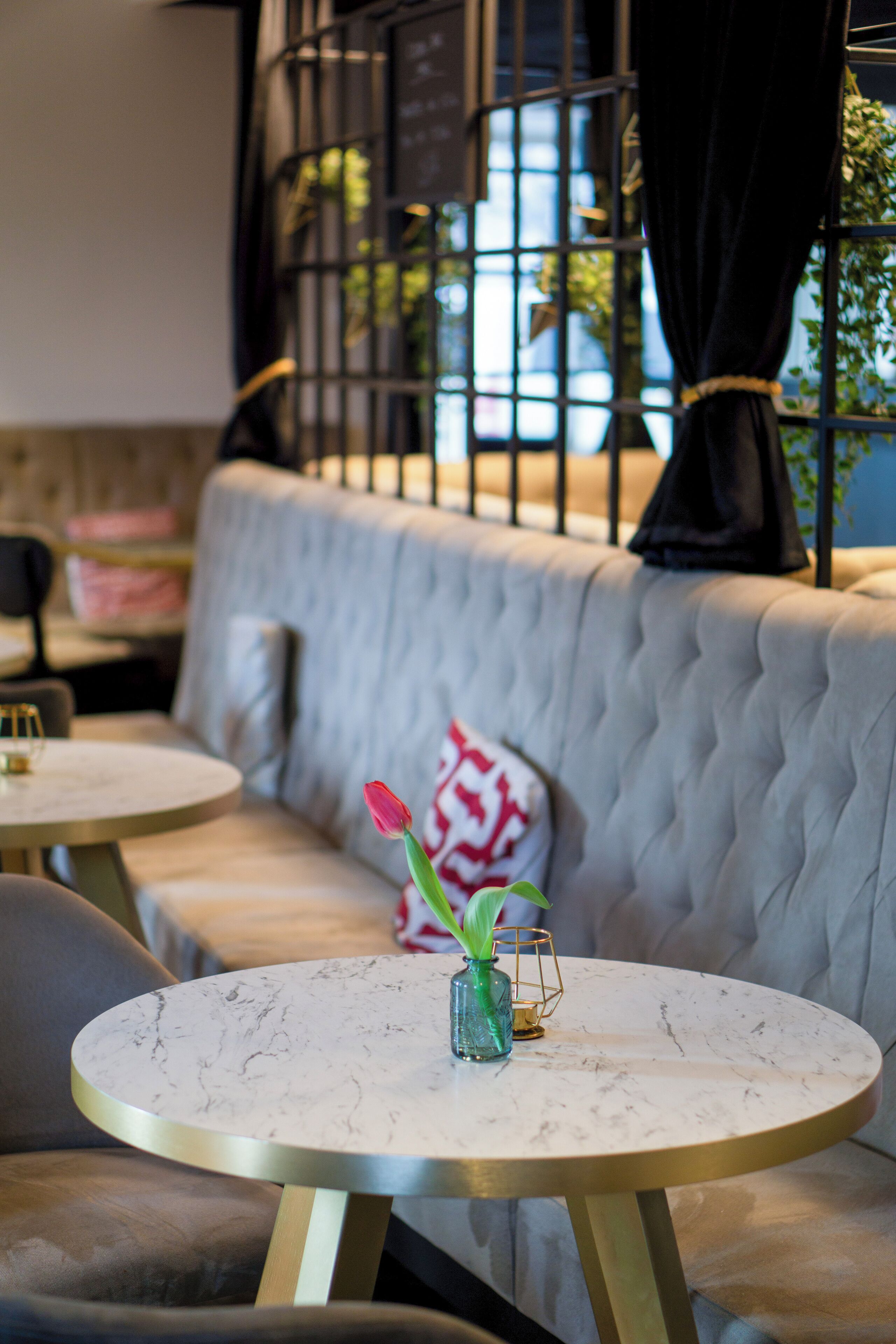 A seating area with a tufted sofa, round tables, and a vase with a red flower.
