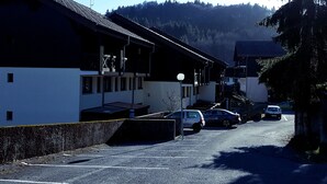A parking lot with several cars, a building with a sloped roof, and a mountain in the background.