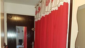 A narrow hallway with a red curtain, a dark wooden door, and a mirror reflecting a bed and a red chair.
