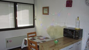 A kitchen with a wooden table, a microwave, a chair, a window with blinds, and a string of colorful lights.