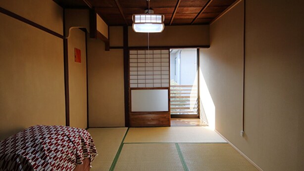 A traditional Japanese room with tatami flooring, a futon bed, sliding shoji doors, and a ceiling fan. - Kyo Maimai (Kyoto)
