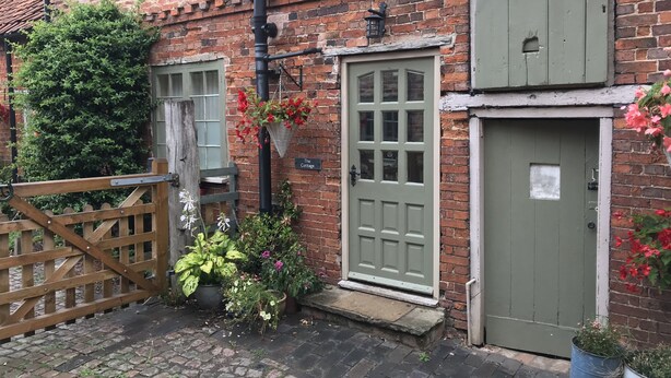 A brick building with a green door, a wooden gate, and various potted plants.