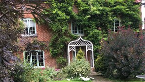 A brick house with a well-maintained garden, a white gazebo, and a brick pathway.