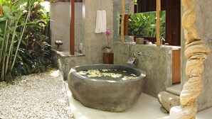 A modern bathroom with a large stone basin, a wooden pergola, and lush greenery. - Dea Villas (Canggu)