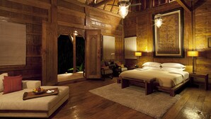 A wooden room with a bed, a sofa, and a dining table with fruit. - Dea Villas (Canggu)