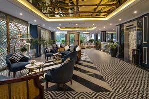 A modern hotel lobby with a geometric patterned floor, seating areas with sofas and armchairs, and a reception desk.