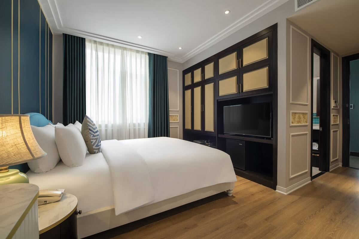 A hotel room with a large bed, a TV, and a desk with a lamp.