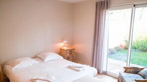 Ein Schlafzimmer mit einem großen Bett, einem Nachttisch mit Lampe, einem Sessel und Blick auf einen Garten durch eine Glastür.