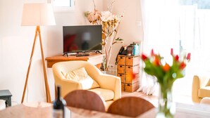 Ein Wohnzimmer mit Fernseher, einer Couch, einer Lampe und einer Blumenvase.