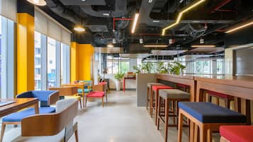 A modern interior with high ceilings, exposed ductwork, and a mix of seating arrangements including bar stools and cushioned chairs.