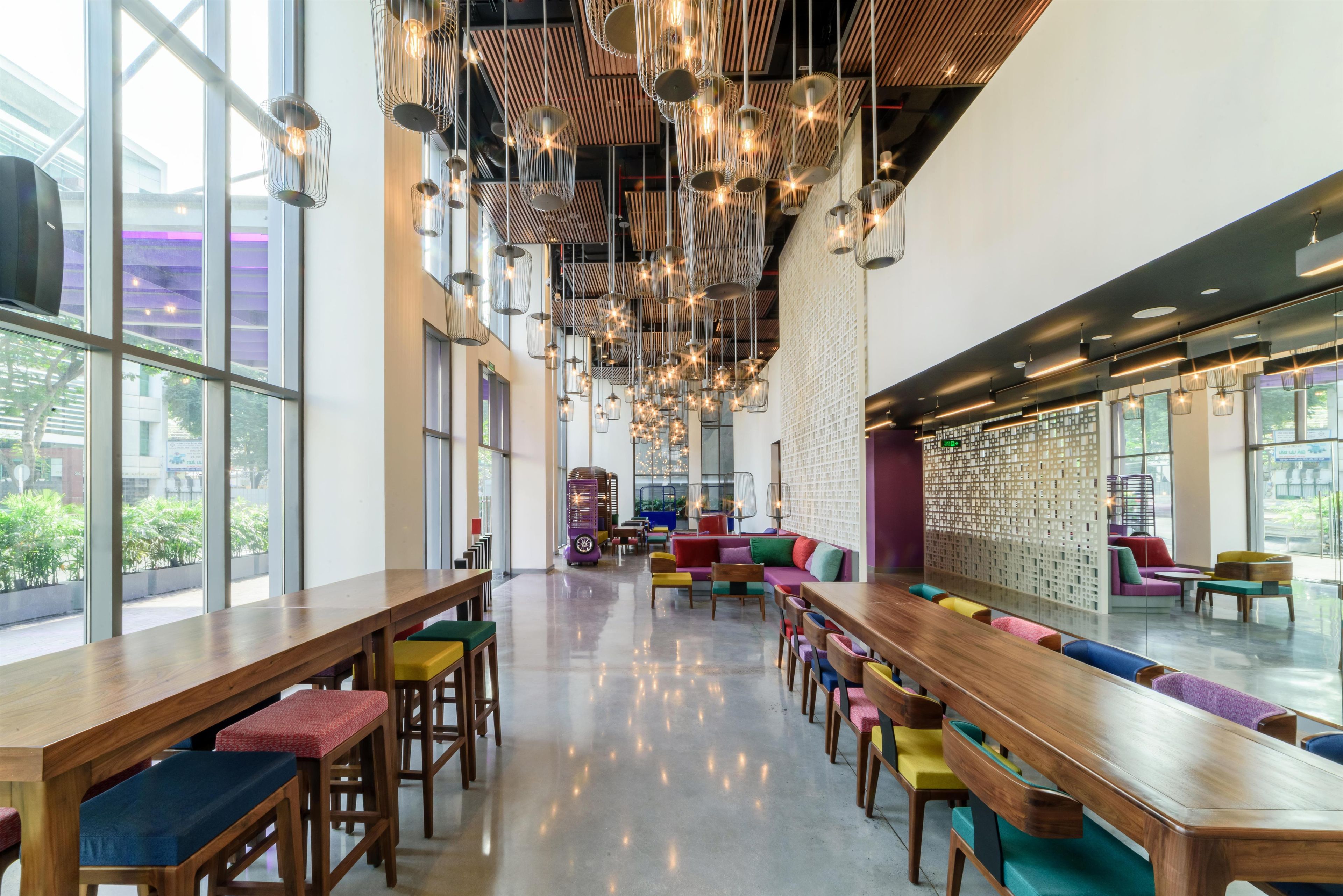 A spacious indoor area with long wooden tables and colorful seating, large windows, and hanging star-shaped lights.