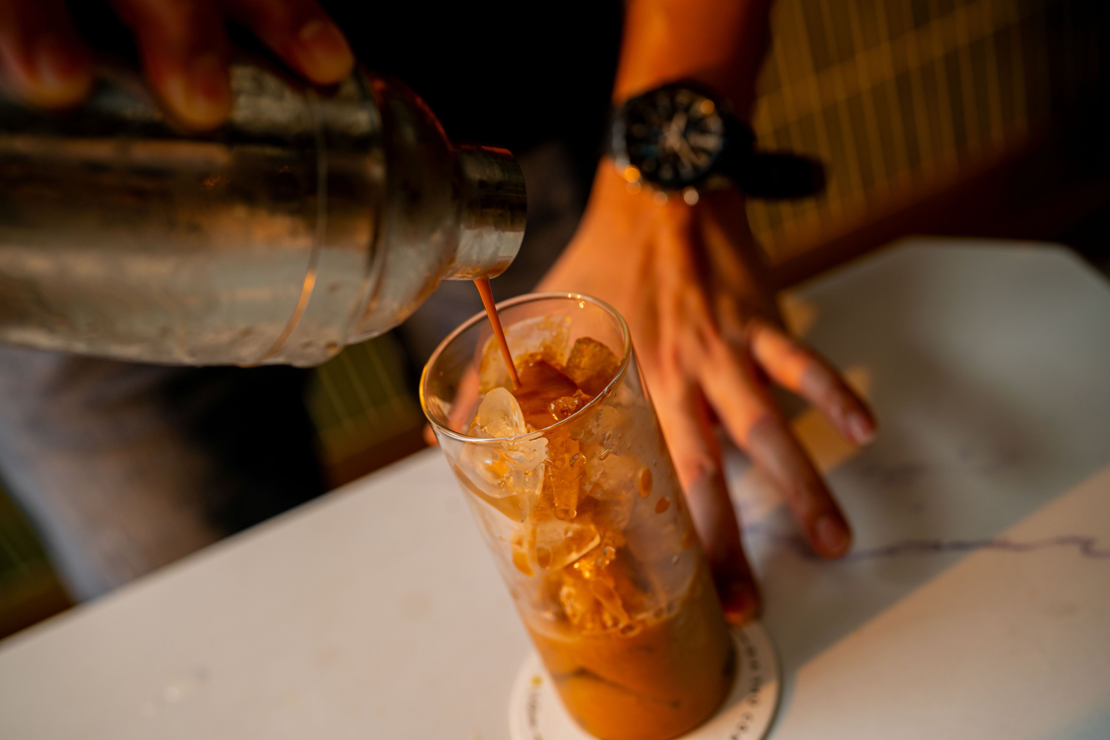A person pouring a drink into a glass with ice cubes.