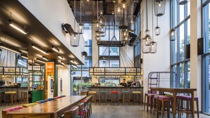Un café espacioso con techos altos, lámparas colgantes y ventanas amplias.