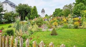 Stroll through the beautifully maintained garden, surrounded by a variety of flowering plants and shrubs, with a traditional building and tower in the background.
