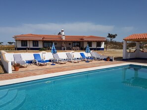 A pool area with lounge chairs and umbrellas, a tiled pool, and a building with a tiled roof in the background. - Spacious luxury country house. Shared pool. Fully wheelchair accessible (Ourique)